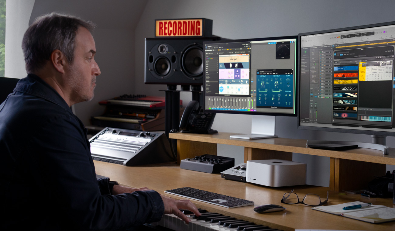 En musiker, der bruger et klaver til at skabe lydmix med Mac Studio og Studio Display